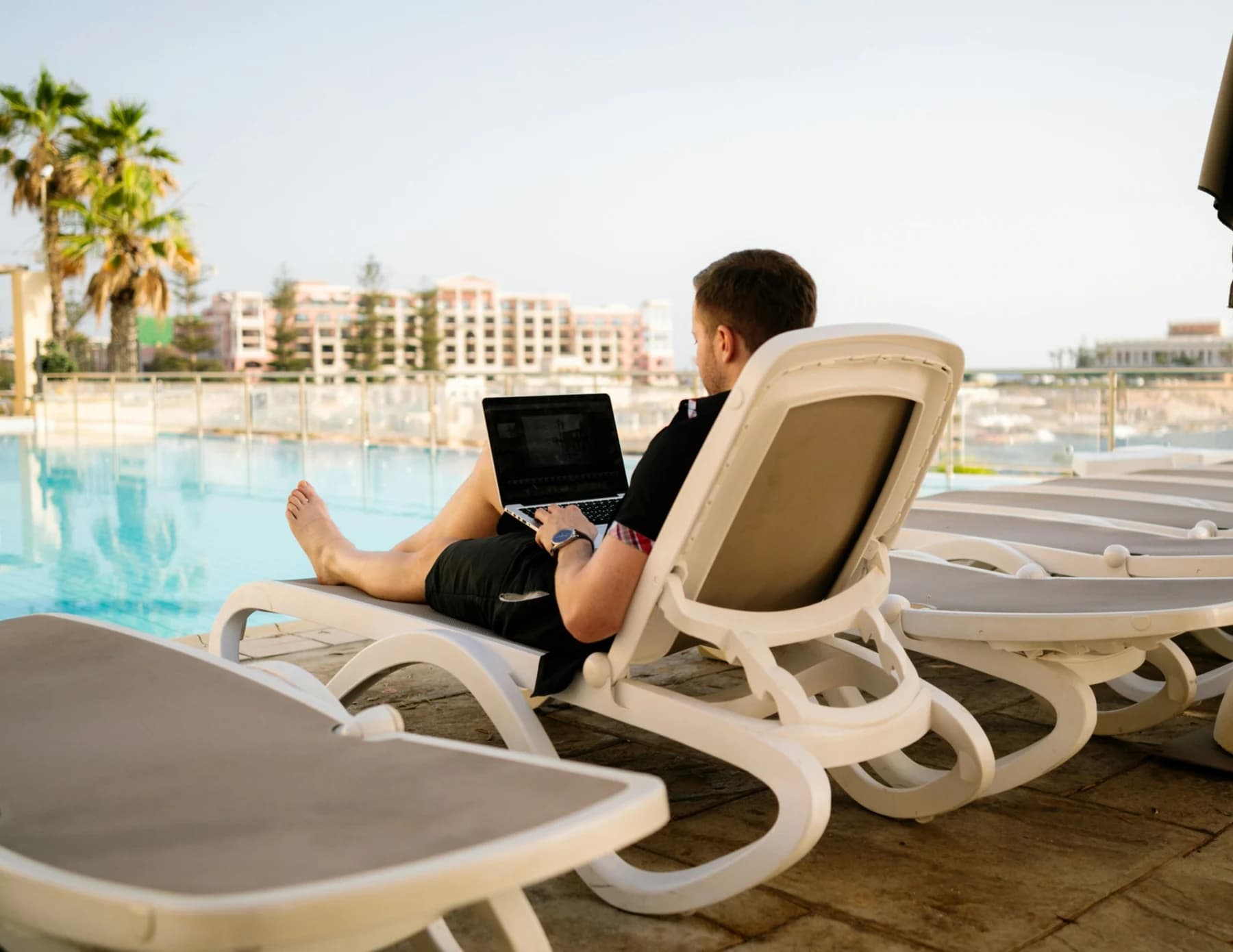 Remote worker using a laptop beside a swimming pool